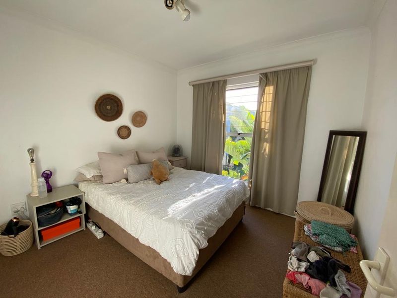 A functional bedroom featuring neutral wall tones, carpeted flooring, and a window with curtain treatments providing natural light.