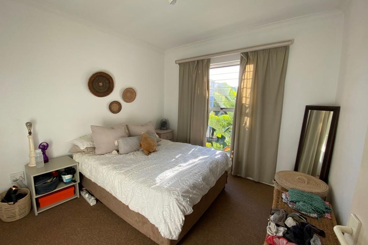 A functional bedroom featuring neutral wall tones, carpeted flooring, and a window with curtain treatments providing natural light.
