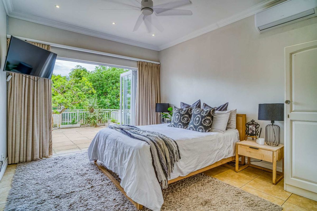 Spacious bedroom featuring tiled flooring, a ceiling fan, wall-mounted air conditioning unit, and large glass doors opening onto a private balcony.
