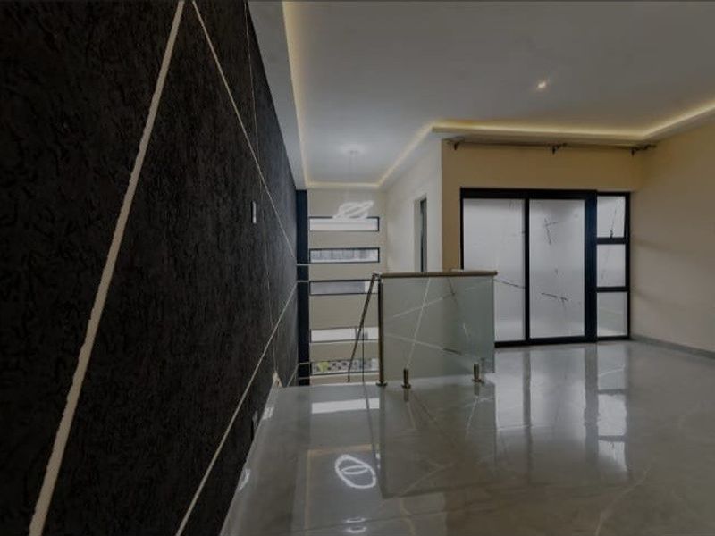 Modern hallway featuring a striking textured feature wall, sleek glass balustrade, recessed ceiling lighting, and polished tiled flooring leading to sliding glass doors.