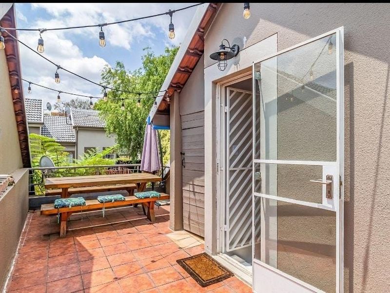 A covered outdoor patio area featuring tiled flooring, a security gate, and overhead string lighting, providing a functional space for outdoor relaxation.
