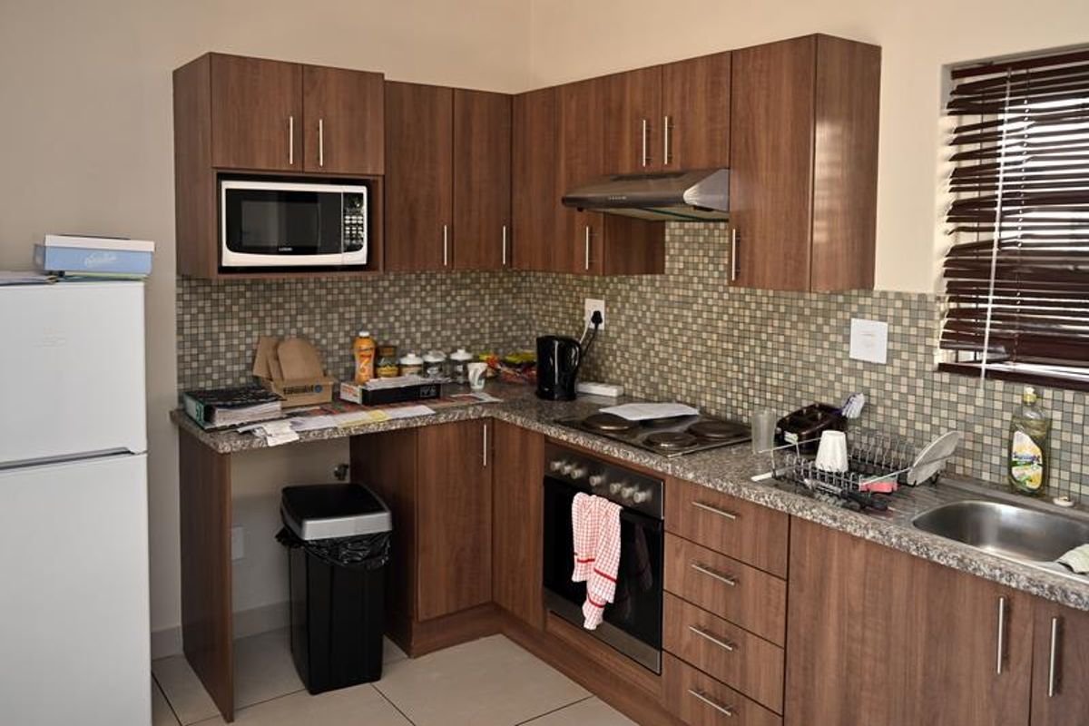 A functional kitchen featuring wood-look cabinetry, a mosaic tile backsplash, built-in oven, hob, and extractor fan with ample counter space.