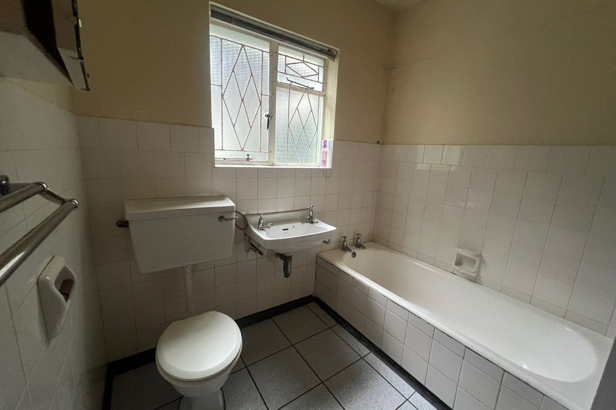 A dated bathroom featuring a standard bathtub, wall-mounted basin, and toilet, with tiled finishes throughout. The space is ready for a modern renovation.