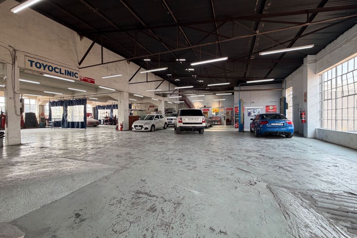 Spacious industrial garage facility featuring high exposed ceilings, large windows for natural light, and durable concrete flooring, currently utilized as an automotive workshop.