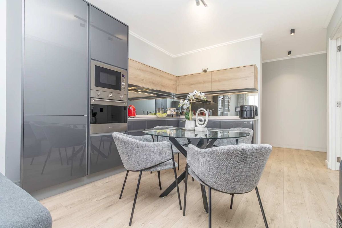 Modern kitchen featuring high-gloss grey cabinetry, wood-tone upper cabinets, a mirrored splashback, and integrated appliances, complemented by light wood-look flooring.
