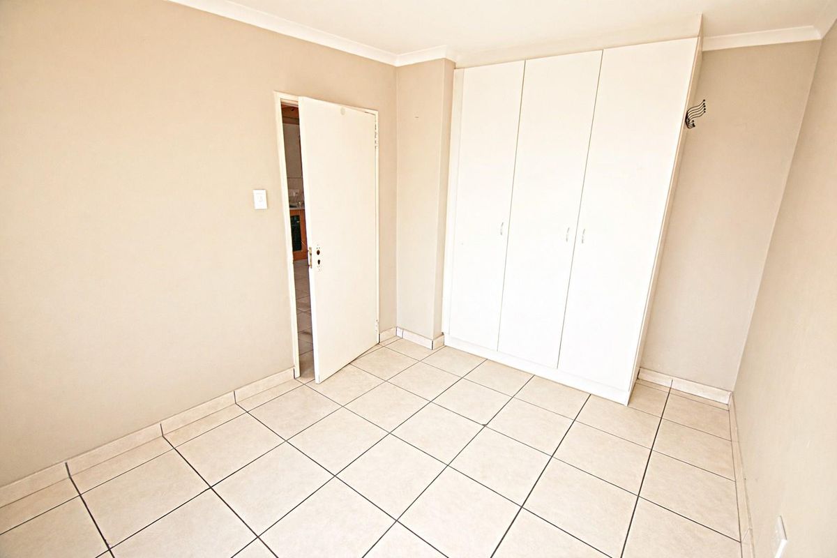 A bright, empty bedroom featuring neutral tiled flooring and built-in white cabinetry, offering a clean and versatile space.