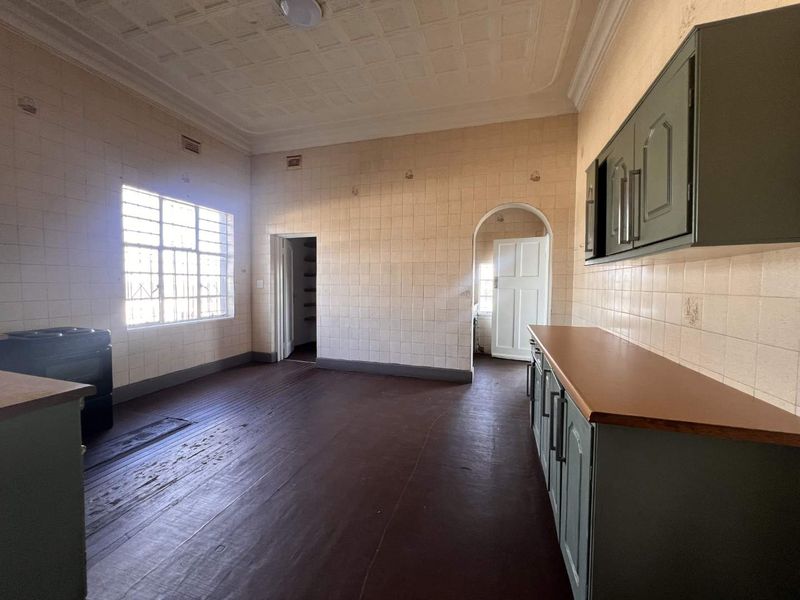 Spacious kitchen featuring original pressed metal ceilings, timber flooring, and dated cabinetry, offering significant potential for a modern renovation.