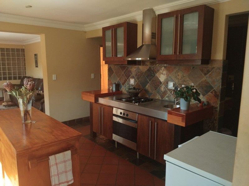 A functional kitchen featuring dark wood cabinetry, a stainless steel countertop with integrated hob and oven, and a stone tile backsplash.