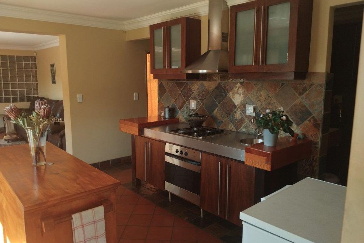 A functional kitchen featuring dark wood cabinetry, a stainless steel countertop with integrated hob and oven, and a stone tile backsplash.