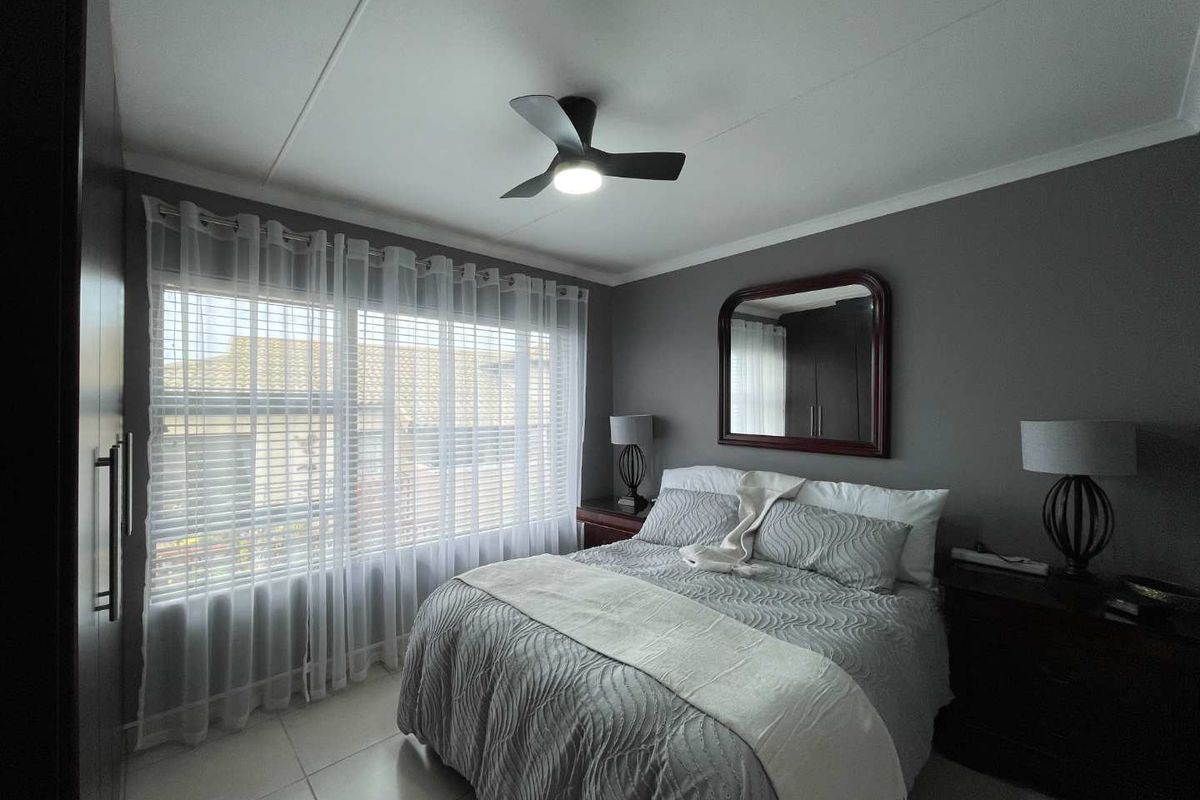A well-maintained bedroom featuring neutral grey walls, tiled flooring, a modern ceiling fan with integrated lighting, and built-in cabinetry.