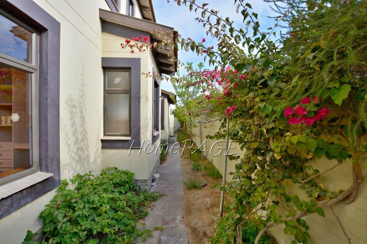 A side walkway along the exterior of the house, featuring paved pathing, boundary wall, and established garden landscaping.