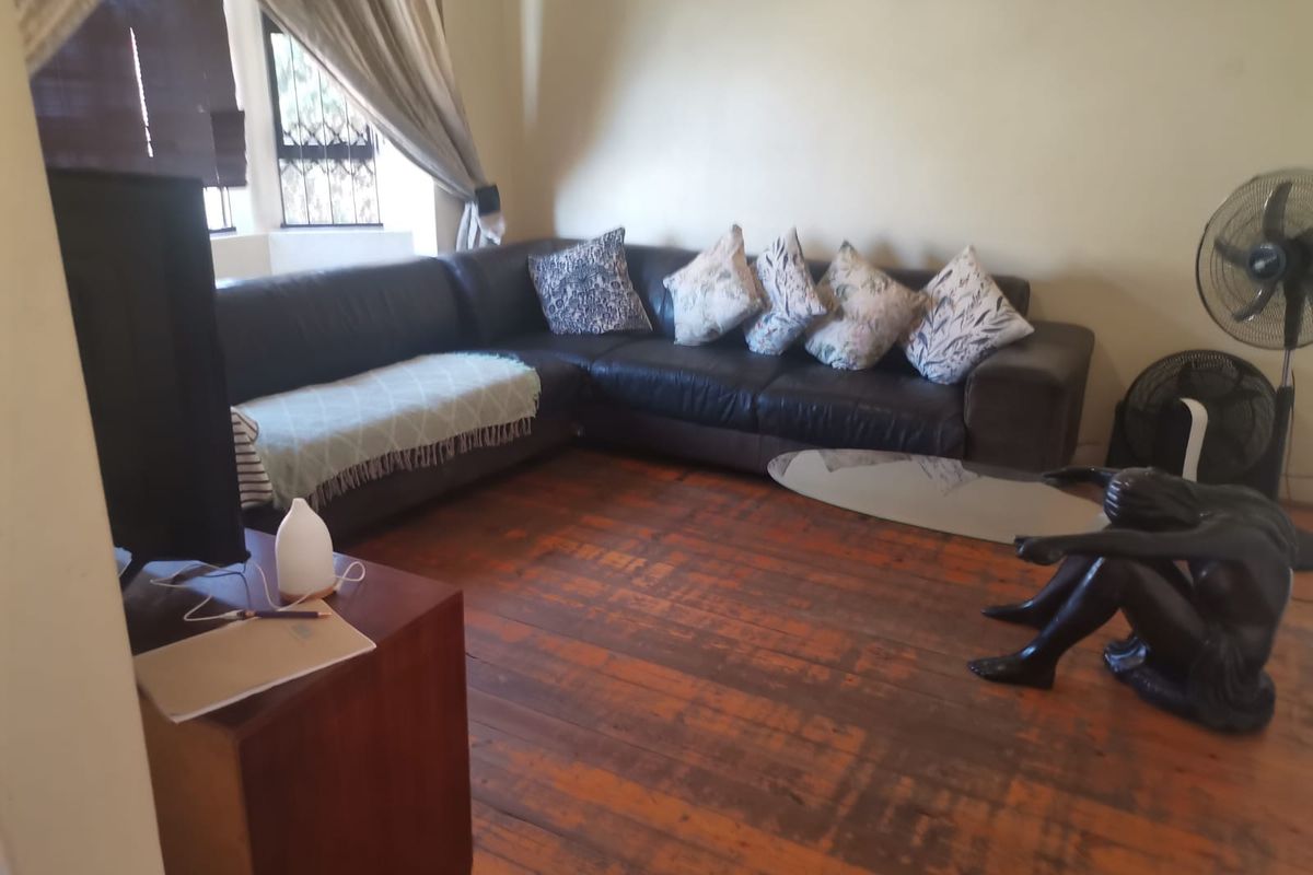 A living room featuring original hardwood flooring and windows fitted with security bars, offering a functional space with potential for cosmetic updates.