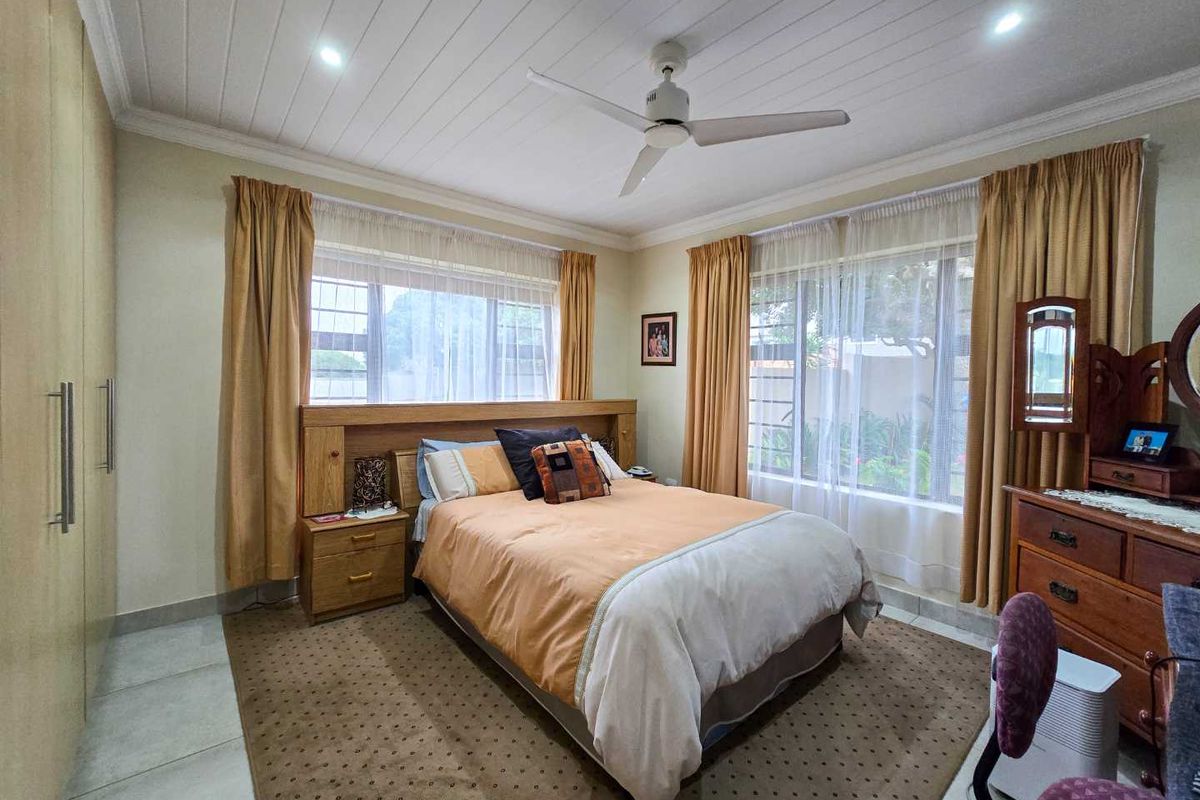 A well-maintained bedroom featuring built-in cupboards, a ceiling fan, and large windows that provide ample natural light.