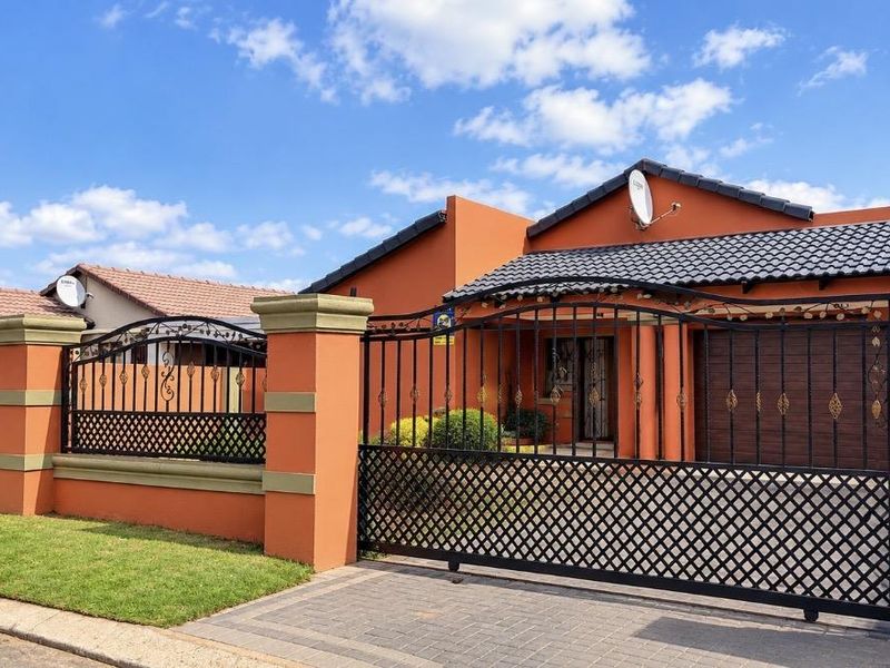 Front elevation of a residential house featuring a paved driveway, secure wrought iron fencing, and a tiled roof.