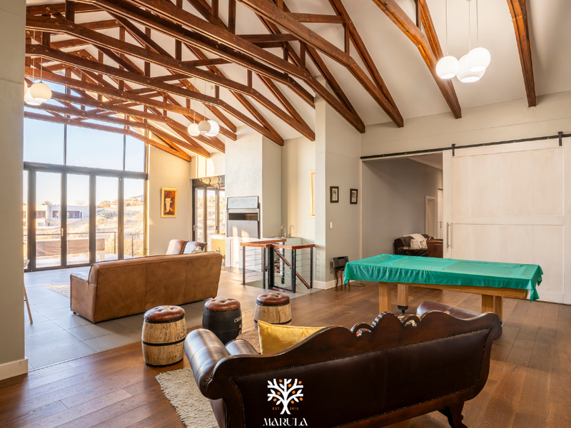 Spacious living area featuring high vaulted ceilings with exposed timber trusses, large glass doors for natural light, and premium hardwood flooring.