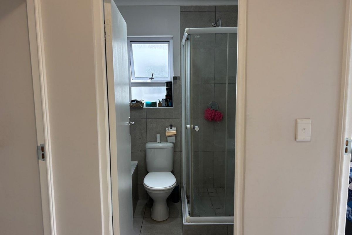 A functional bathroom featuring a glass-enclosed shower, a standard toilet, and tiled wall finishes with a small window for natural light.