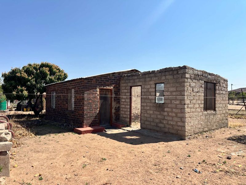 A single-story residential structure featuring a combination of exposed brick and unfinished concrete block construction with a metal roof.