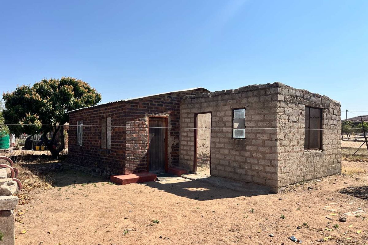 A single-story residential structure featuring a combination of exposed brick and unfinished concrete block construction with a metal roof.
