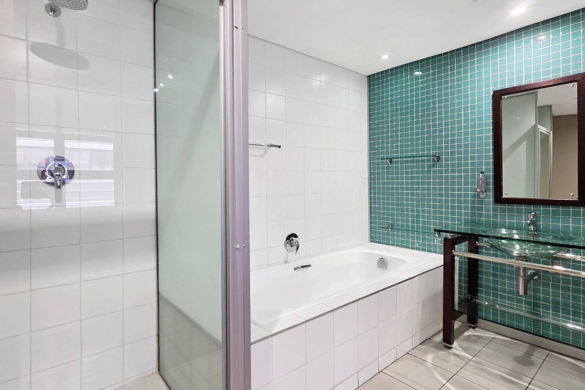 Modern bathroom featuring a glass-enclosed shower, a built-in bathtub, and a glass basin vanity with teal mosaic tile accents.