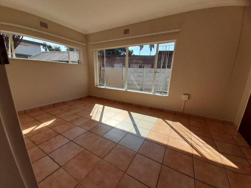 A bright, empty living room featuring ceramic floor tiles and large windows with security bars, offering a blank canvas for interior design.