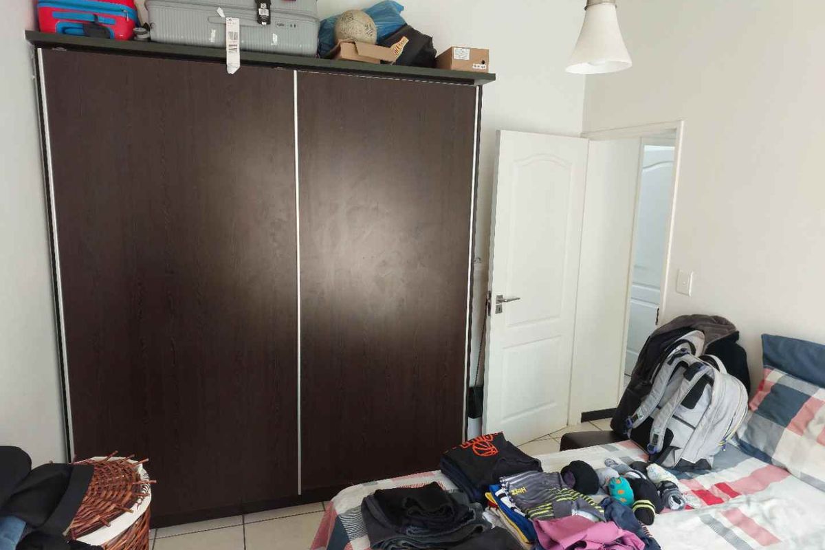A bedroom featuring tiled flooring and a built-in dark wood wardrobe, providing functional storage space within the apartment.