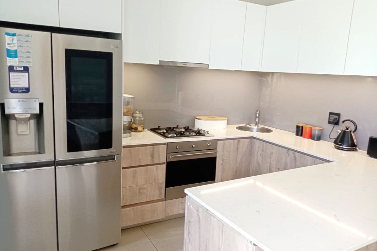 Modern kitchen featuring stone countertops, light wood-grain cabinetry, built-in oven, gas hob, and a stainless steel sink with a sleek glass splashback.