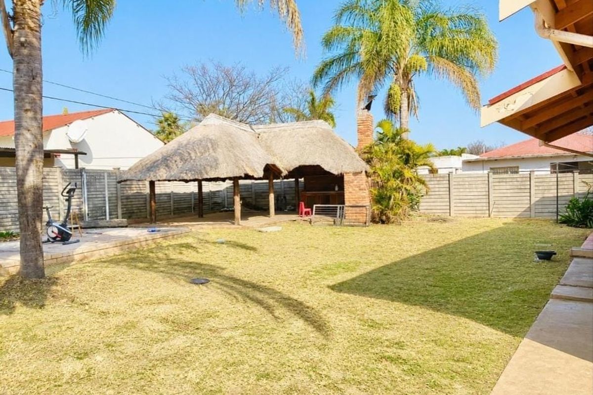Spacious rear garden featuring a thatched lapa with a built-in brick braai, paved patio area, and perimeter precast walling.