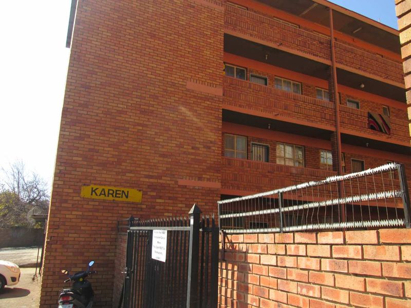 Exterior view of the Karen apartment complex featuring a face brick facade, multi-level balconies, and secure perimeter fencing with gated access.