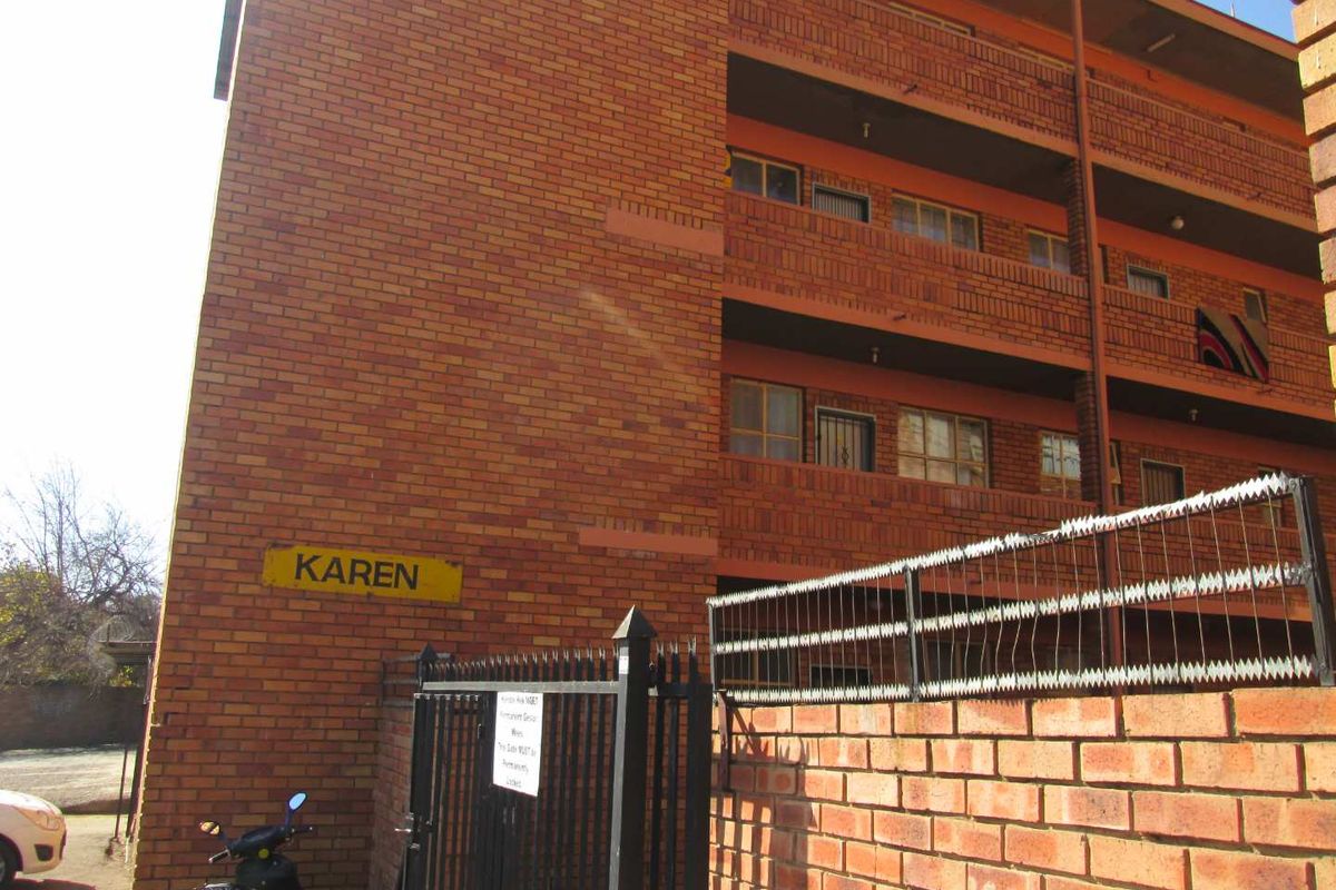 Exterior view of the Karen apartment complex featuring a face brick facade, multi-level balconies, and secure perimeter fencing with gated access.