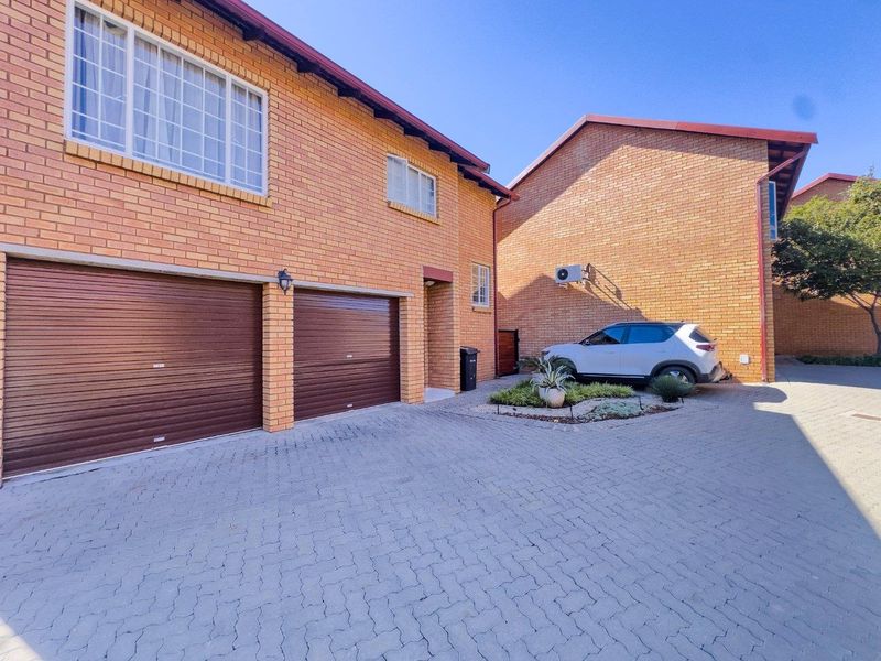 Front view of a townhouse featuring a double garage with roller doors, brick exterior, and a paved driveway.