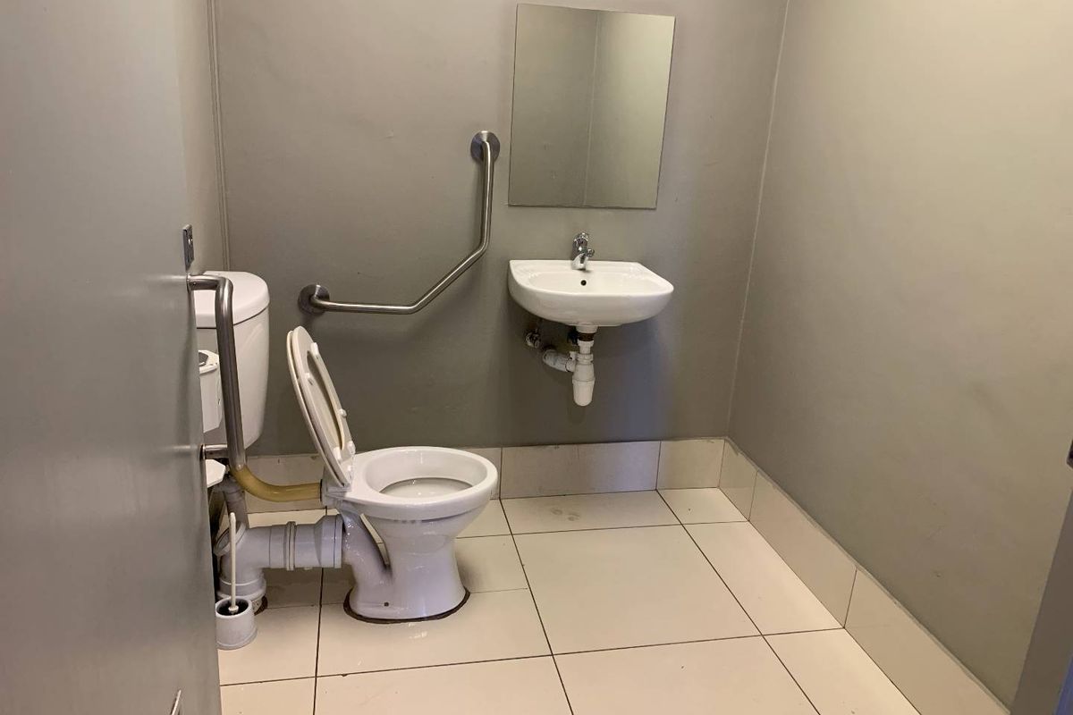 A functional accessible restroom featuring a wall-mounted basin, toilet with grab rails, and tiled flooring.