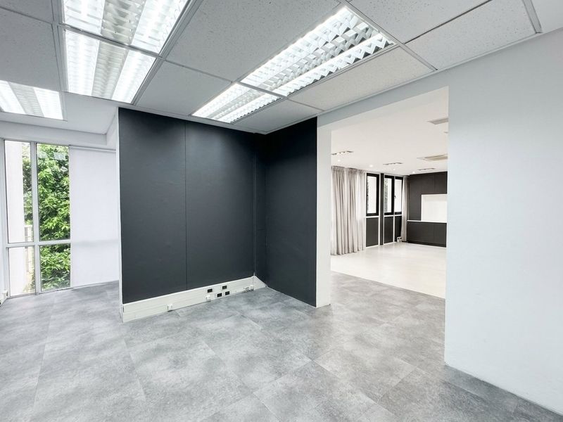 A bright, modern office space featuring tiled flooring, suspended ceilings with recessed lighting, and large windows providing natural light.