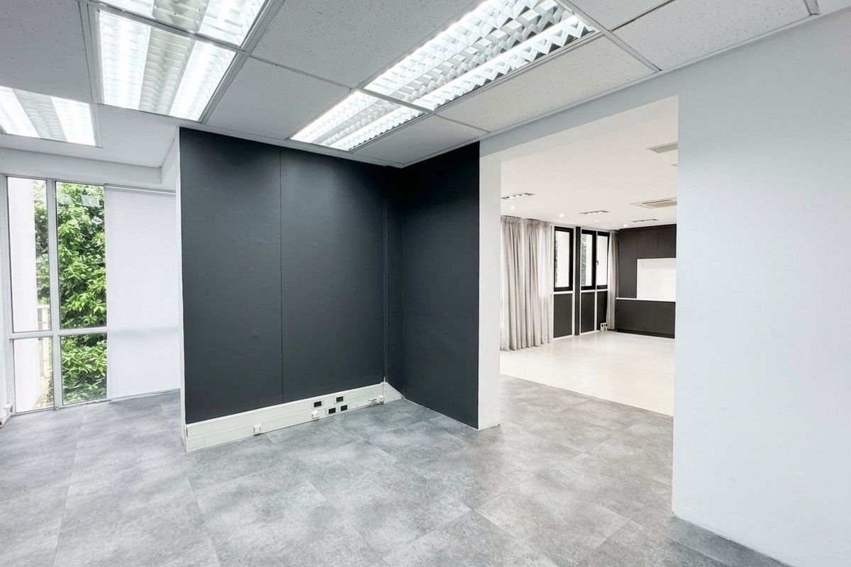 A bright, modern office space featuring tiled flooring, suspended ceilings with recessed lighting, and large windows providing natural light.