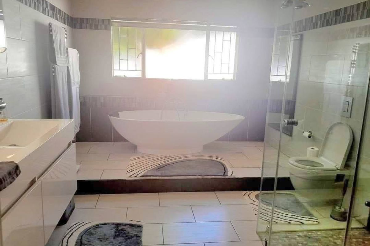 Modern bathroom featuring a freestanding bathtub, glass-enclosed shower, wall-mounted vanity, and neutral tiled finishes throughout.