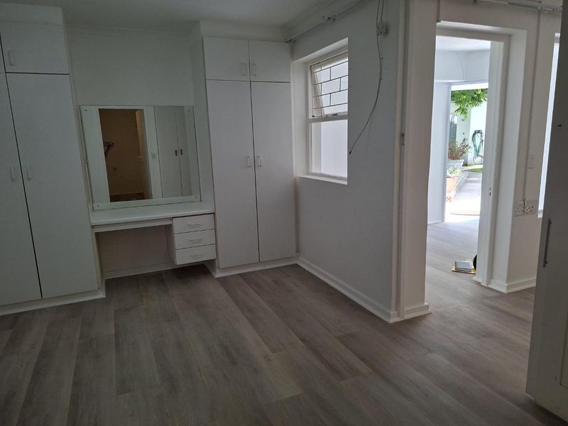 A bright, empty bedroom featuring modern laminate flooring, built-in cupboards, and a integrated vanity unit, with direct access to an outdoor area.