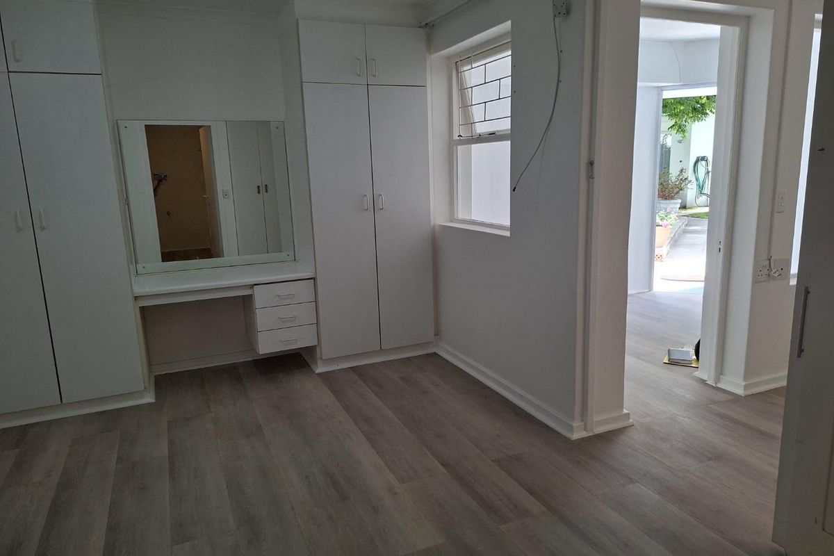 A bright, empty bedroom featuring modern laminate flooring, built-in cupboards, and a integrated vanity unit, with direct access to an outdoor area.
