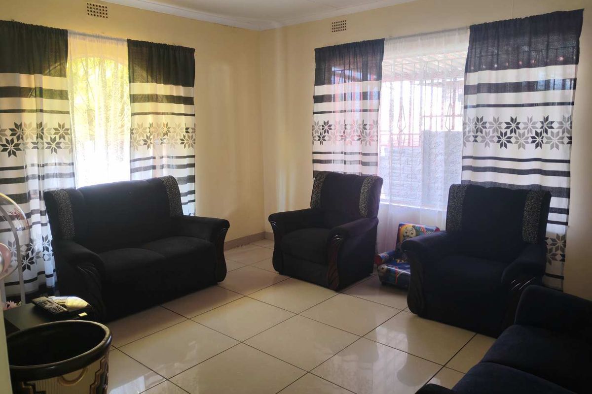 A living room featuring ceramic floor tiles, large windows with security bars, and neutral wall finishes.