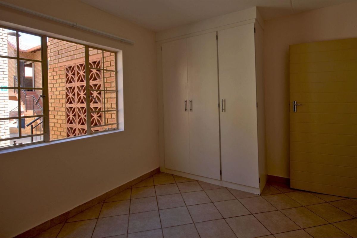 A bright, empty bedroom featuring tiled flooring and a built-in wardrobe, offering a clean canvas for personalization.