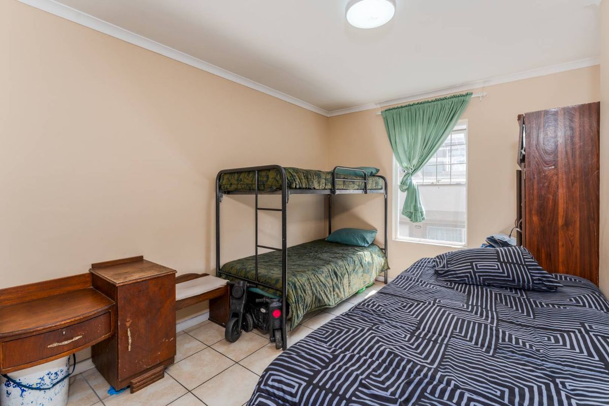 A functional bedroom featuring tiled flooring, a window with curtain, and built-in storage space.