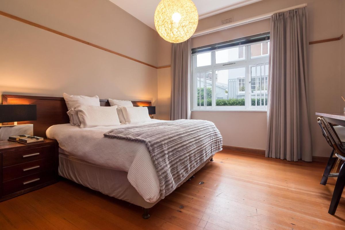 A well-lit bedroom featuring polished wooden flooring, a large window with curtain tracks, and a built-in picture rail.