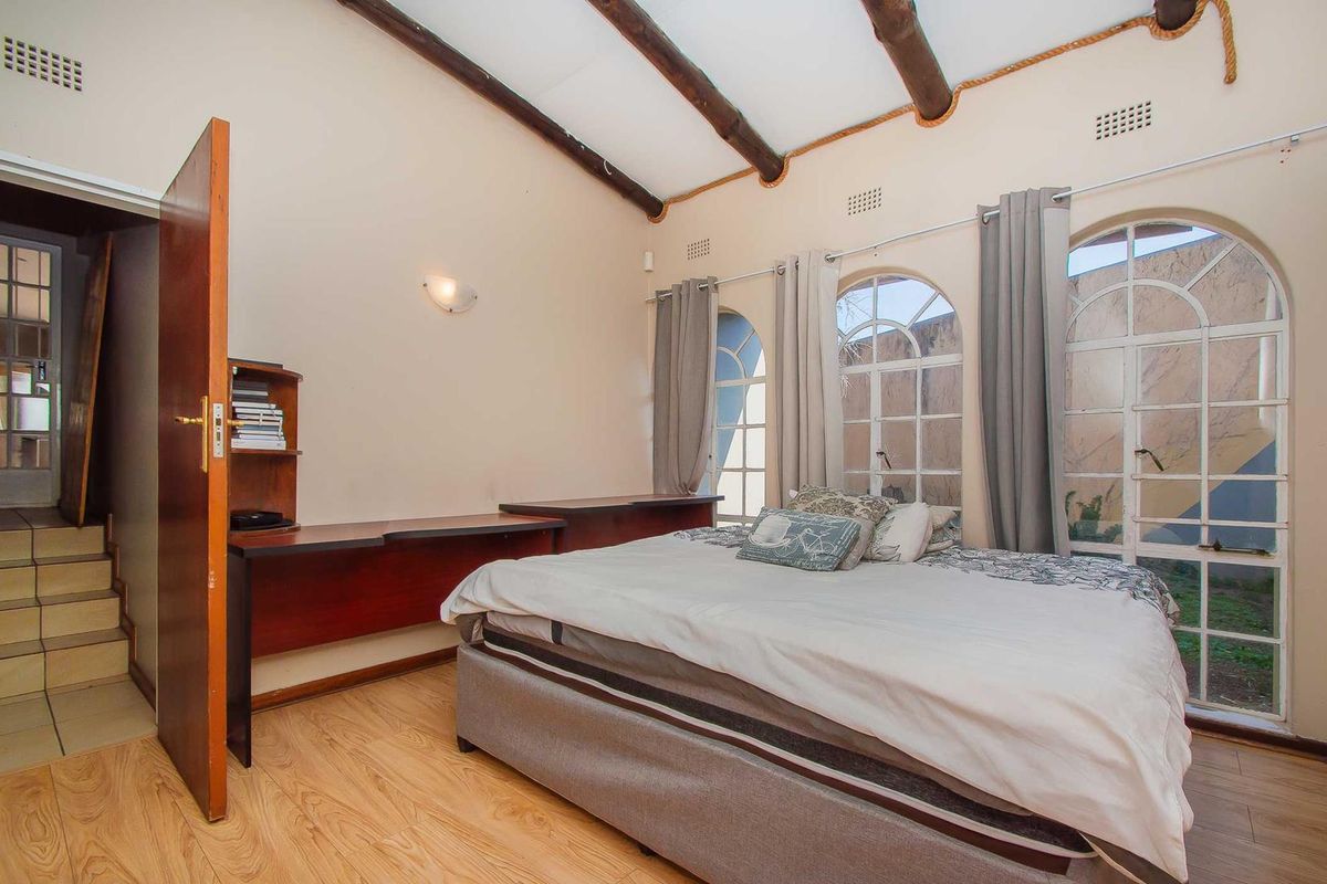 Bedroom featuring exposed timber ceiling beams, arched windows, and a built-in desk, with laminate flooring and direct access to an adjacent hallway.