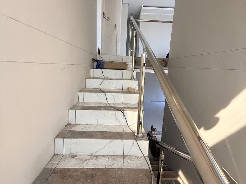 A staircase under construction featuring tiled steps and a stainless steel handrail, currently in a raw, unfinished state.