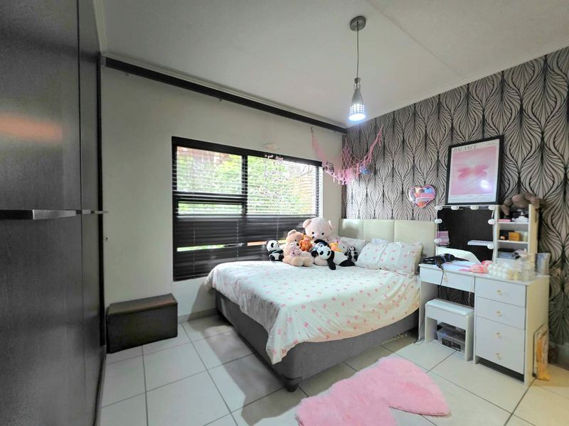 A well-maintained bedroom featuring tiled flooring, built-in cupboards, and a large window with venetian blinds, providing ample natural light.
