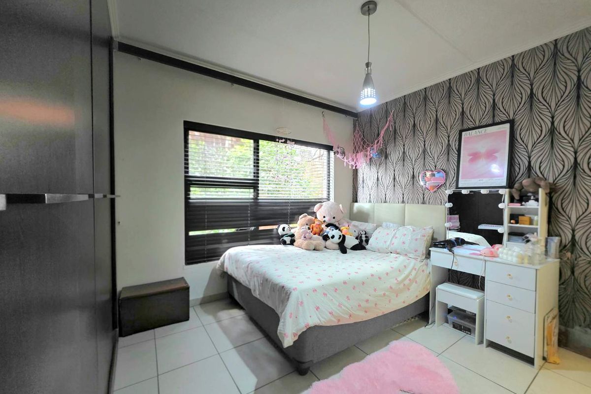 A well-maintained bedroom featuring tiled flooring, built-in cupboards, and a large window with venetian blinds, providing ample natural light.