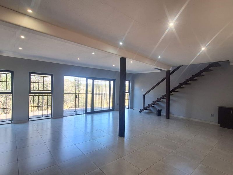 Spacious open-plan living area featuring tiled floors, recessed lighting, a modern steel staircase, and large sliding doors leading to an outdoor space.