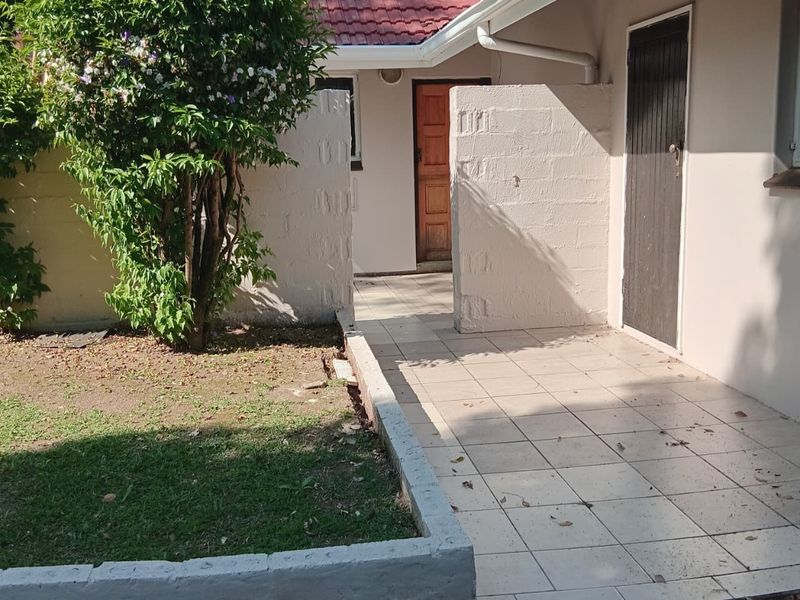 A rear exterior view featuring a tiled patio area, concrete block privacy walls, and a small garden bed with a tiled roof structure.