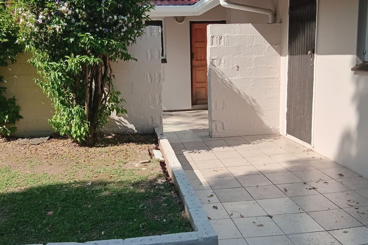 A rear exterior view featuring a tiled patio area, concrete block privacy walls, and a small garden bed with a tiled roof structure.
