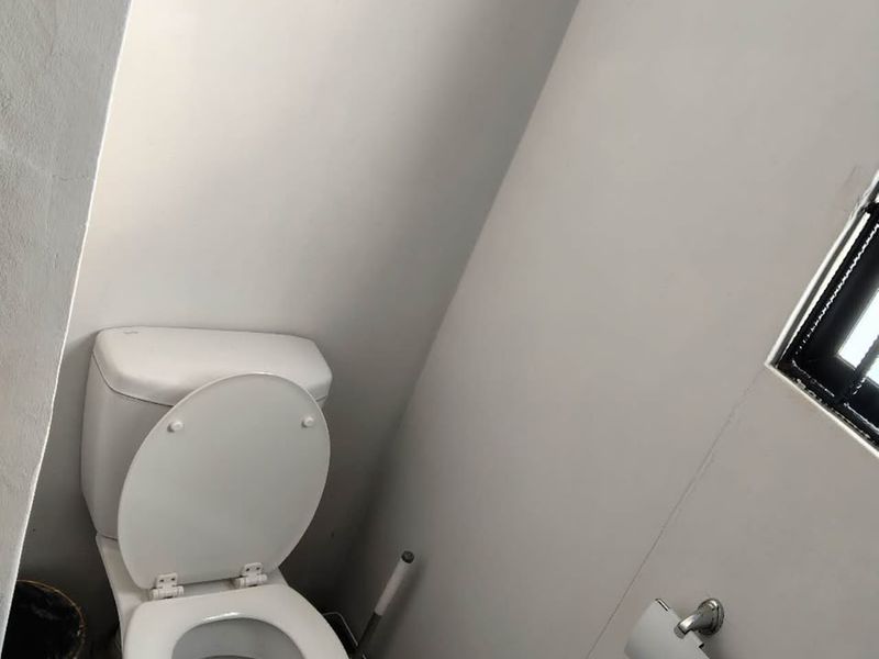 A small, functional bathroom featuring a standard toilet and window, currently requiring floor finishing to complete the space.