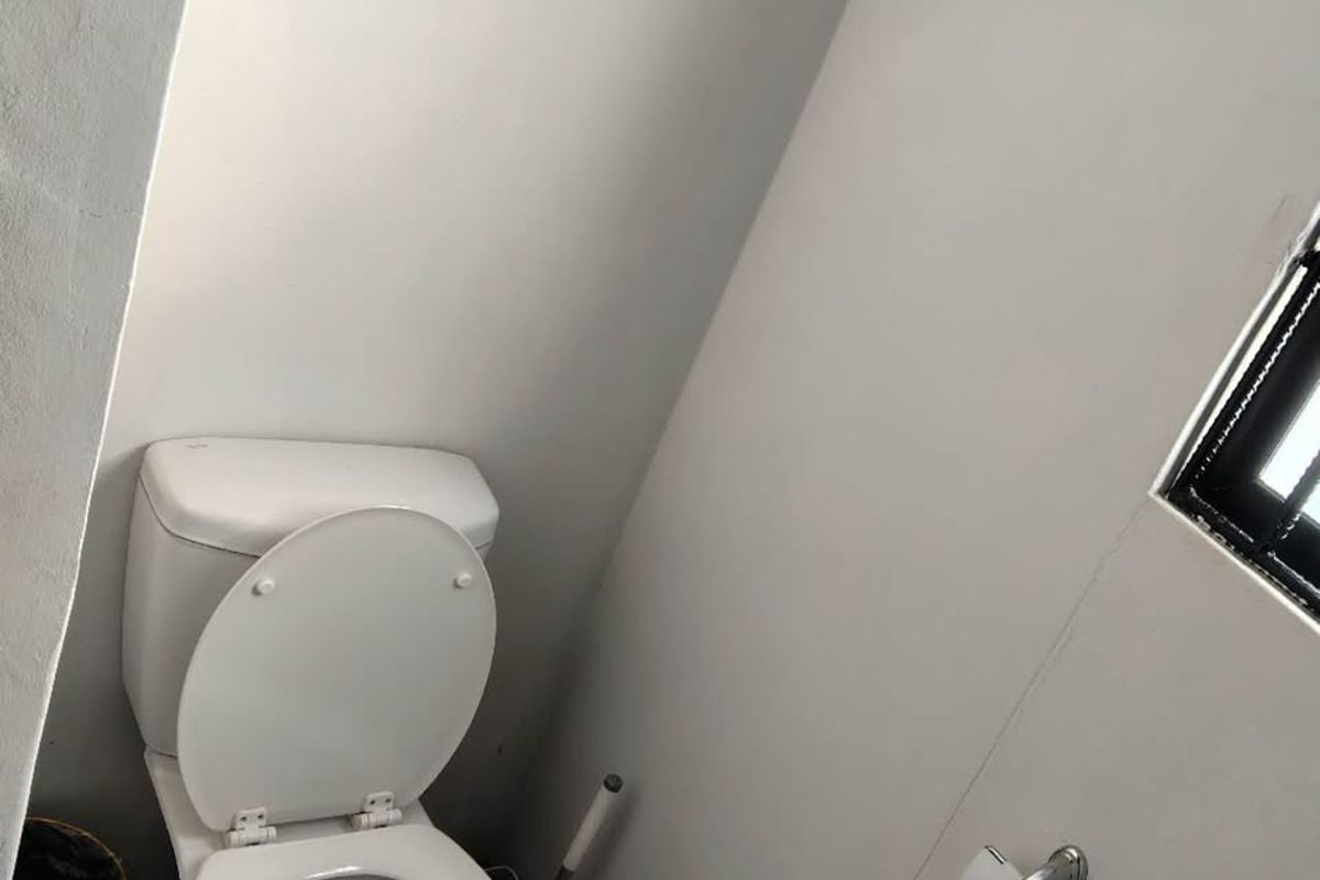 A small, functional bathroom featuring a standard toilet and window, currently requiring floor finishing to complete the space.