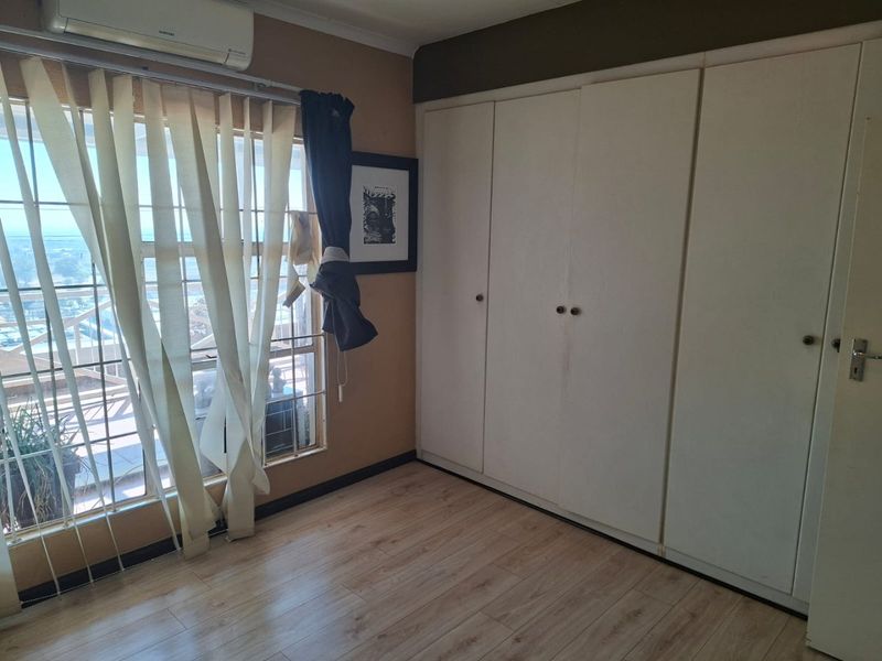 A bedroom featuring light laminate flooring, built-in cupboards, and a wall-mounted air conditioning unit with access to an outdoor balcony area.